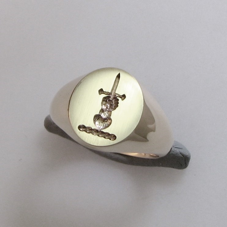 Hand holding dagger above heart crest engraved signet ring